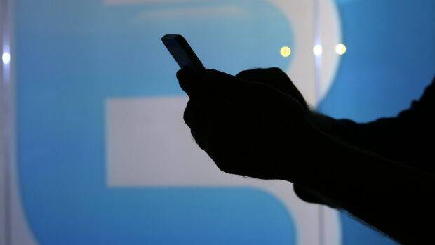 A man checks his mobile phone near a Twitter logo in London. Photo: Bloomberg