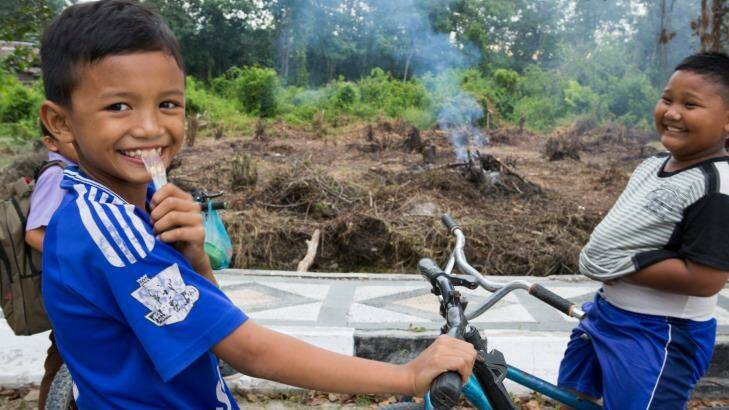 Children ride their bicycles in Pelalawan, in Riau province as small fires burn in the background.  Photo: Rodrigo Ordonez